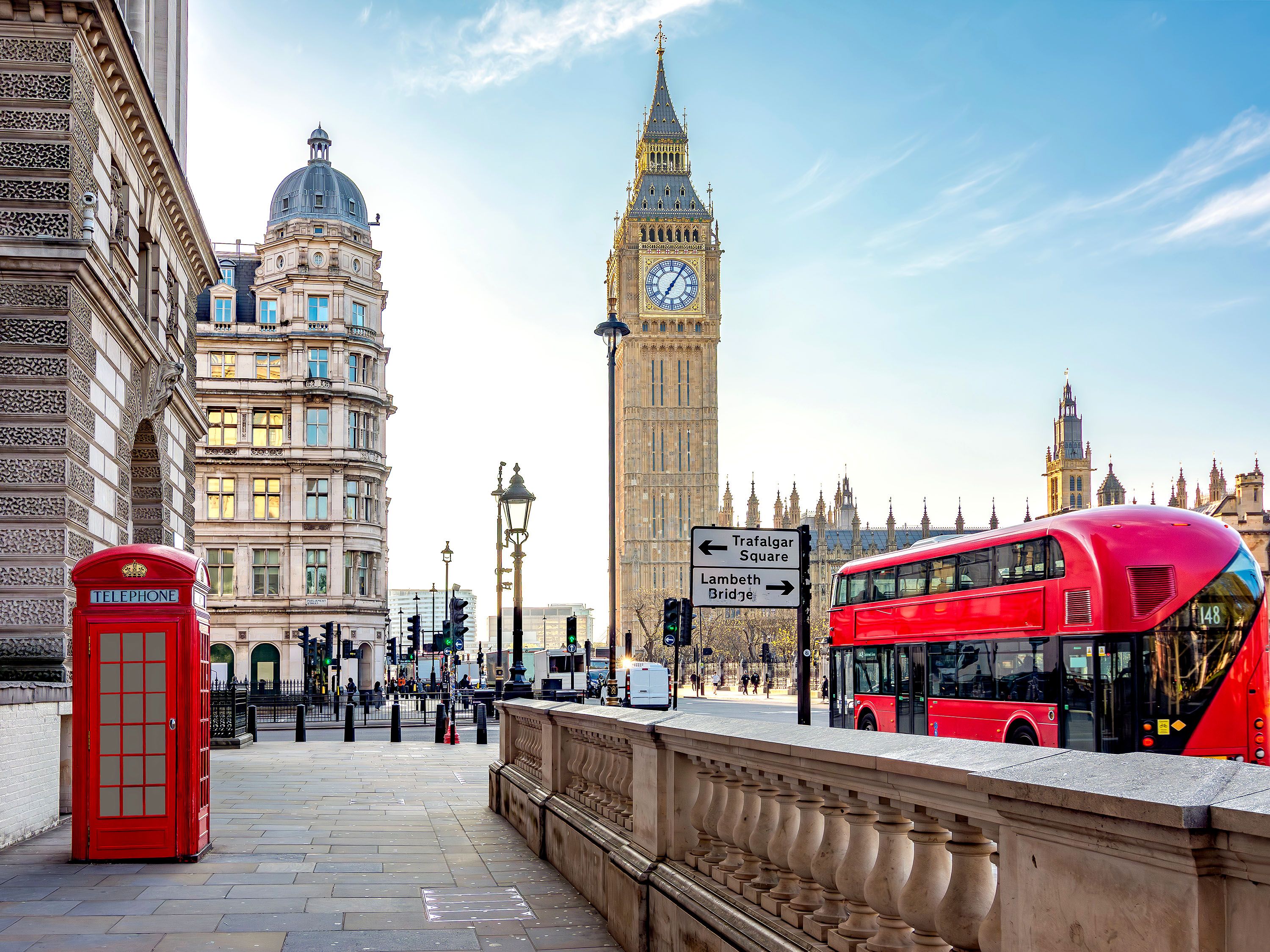 Red phone booth with signs to Trafalgar Square, Big Ben clock tower and red double decker bus.