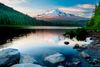 A landscape view of rocks in the foreground of a lake and a snow capped mountain in the distance.