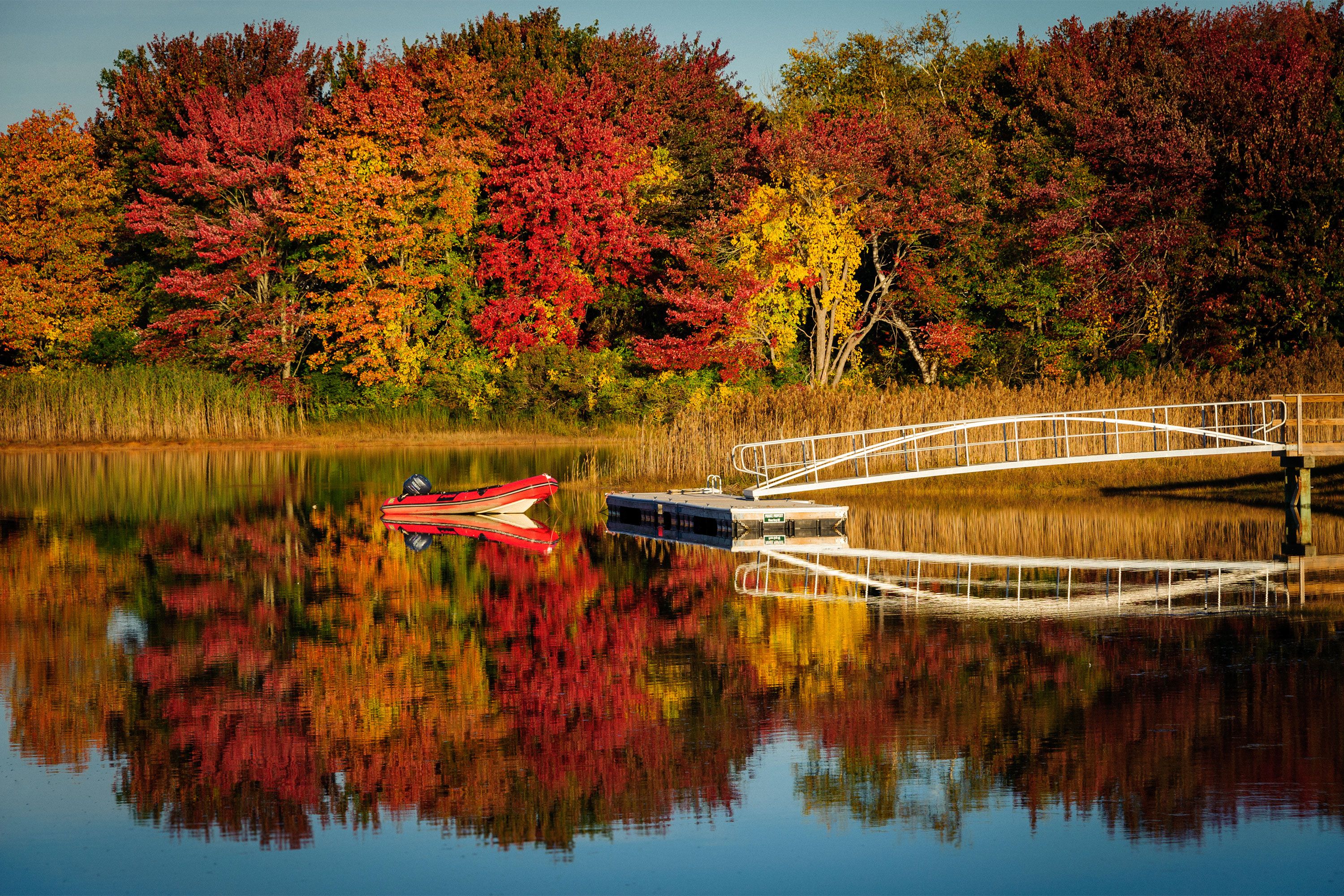 A rowboat on a calm lake in coastal Maine, surrounded by trees with bright fall foliage in red, orange and yellow hues.