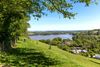 Trees tower over a sloping green gill overlooking cottages and water.