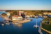 An aerial view of Harbour Town on Hilton Head Island, showing a red-and-white striped lighthouse beside a marina, with surrounding water, docks, boats, and coastal landscape under daylight.