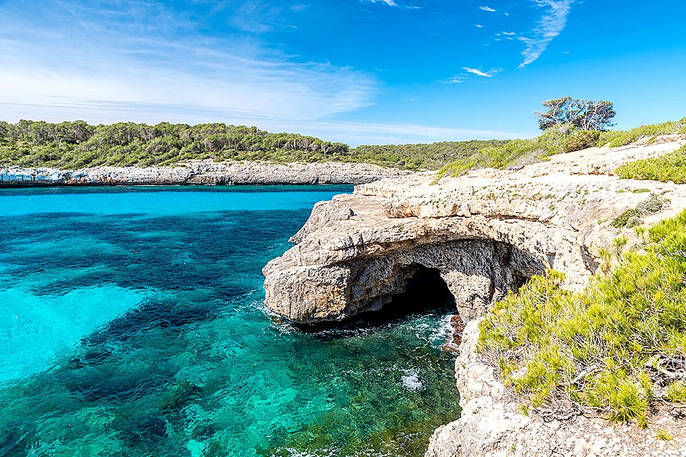 A sea cave surrounded by blue sea and rocky cliffs.