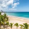 A sandy beach in San Juan, Puerto Rico, with palm trees, blue waters and the city skyline visible in the distance