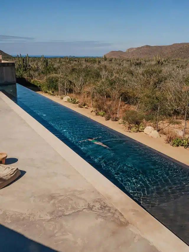 A woman swims in the infinity pool at Paradero Todos Santos, featuring modern architecture, desert landscape, mountains and a hint of ocean in the distance, and a blue sky above