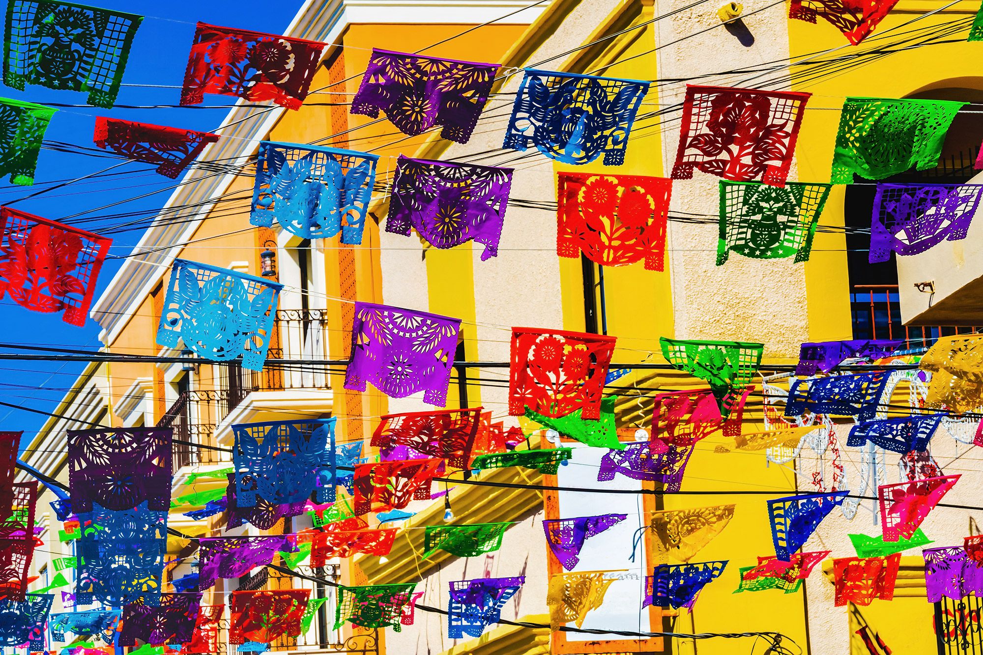Colorful paper flags flying in front of a yellow building in downtown Cabo San Lucas.