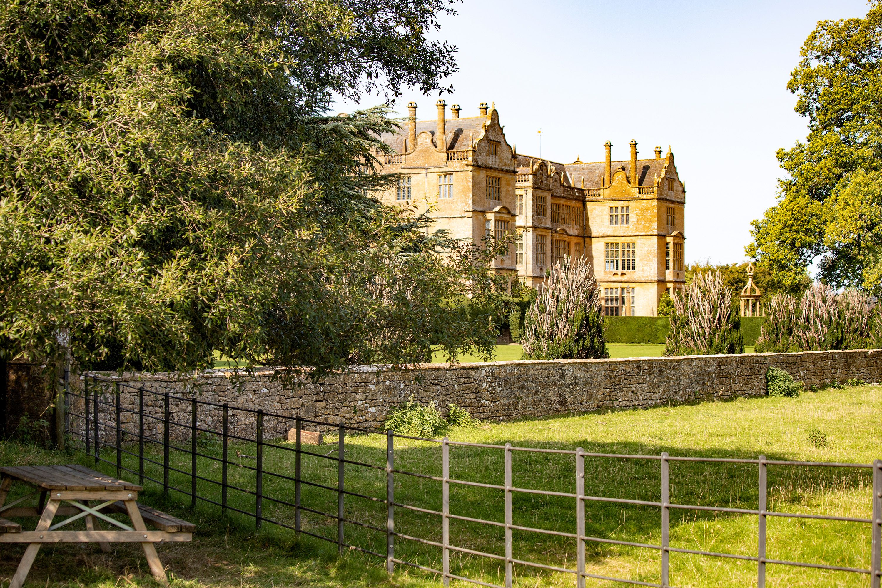 Picnic table and gate surround a large home in the English countryside.