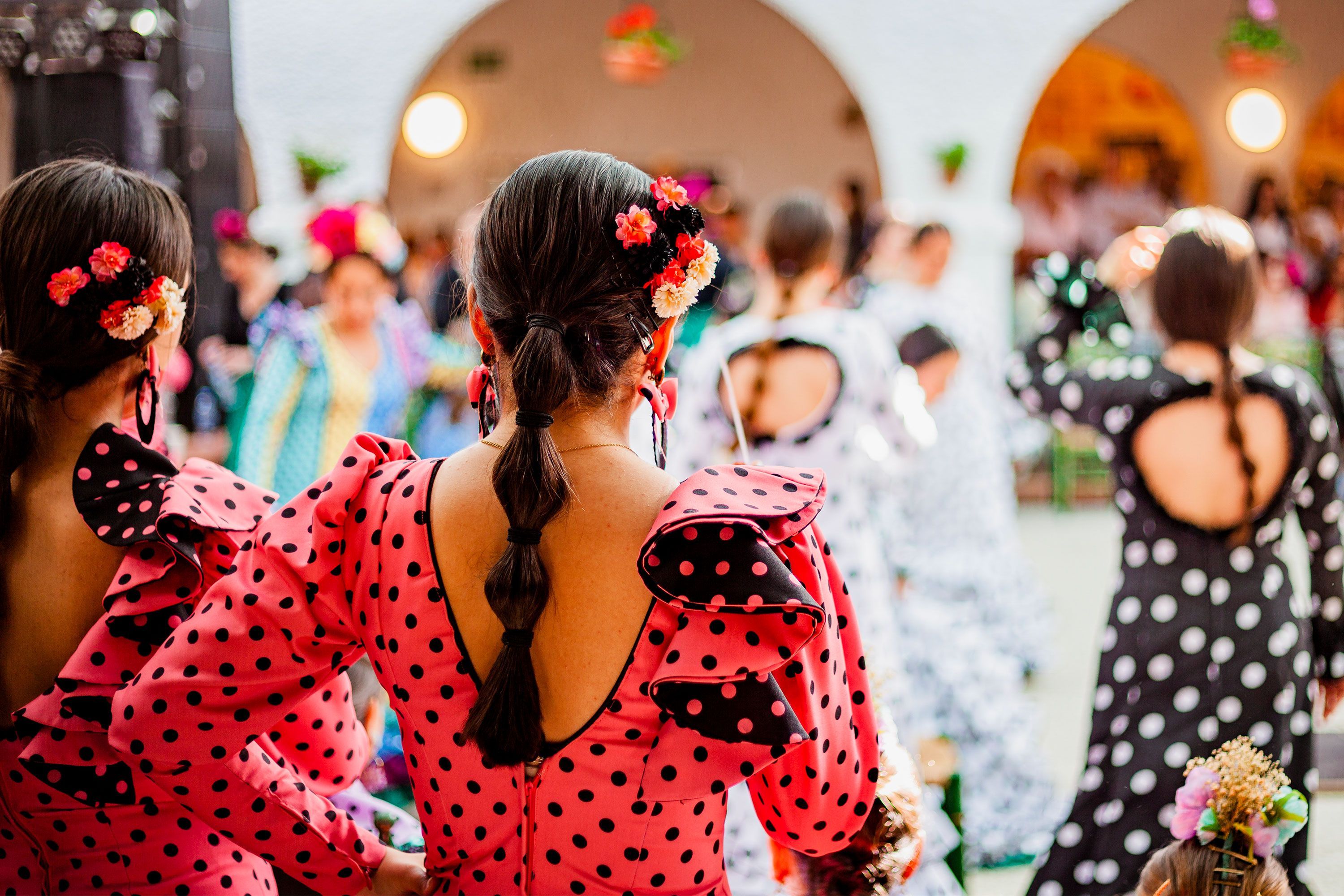 Spanish woman wearing a red and white polka-dot flamenco dress with ruffled sleeves and holding castanets, standing outdoors at a traditional festival in Rota, Spain.