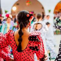 Spanish woman wearing a red and white polka-dot flamenco dress with ruffled sleeves and holding castanets, standing outdoors at a traditional festival in Rota, Spain.