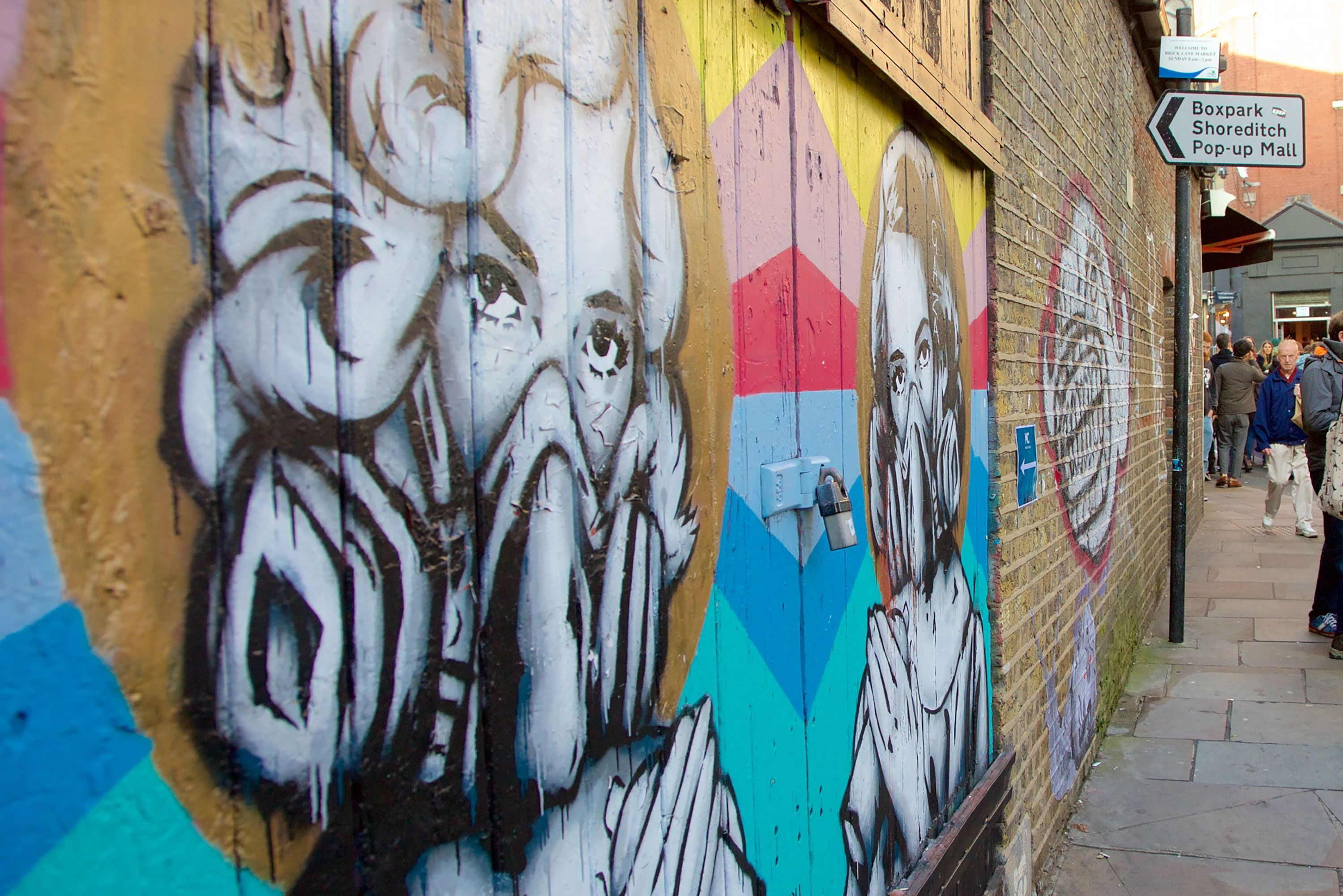 Street art murals line a brick wall near Boxpark Shoreditch in London.