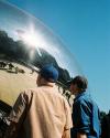 Two men wearing baseball caps look at the reflections in The Bean, a silver bean-shaped sculpture officially known as Cloud Gate, in Chicago