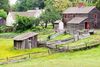 A historic colonial-style farmhouse with adjacent outbuildings surrounded by verdant grass and mature trees under a soft, natural light.
