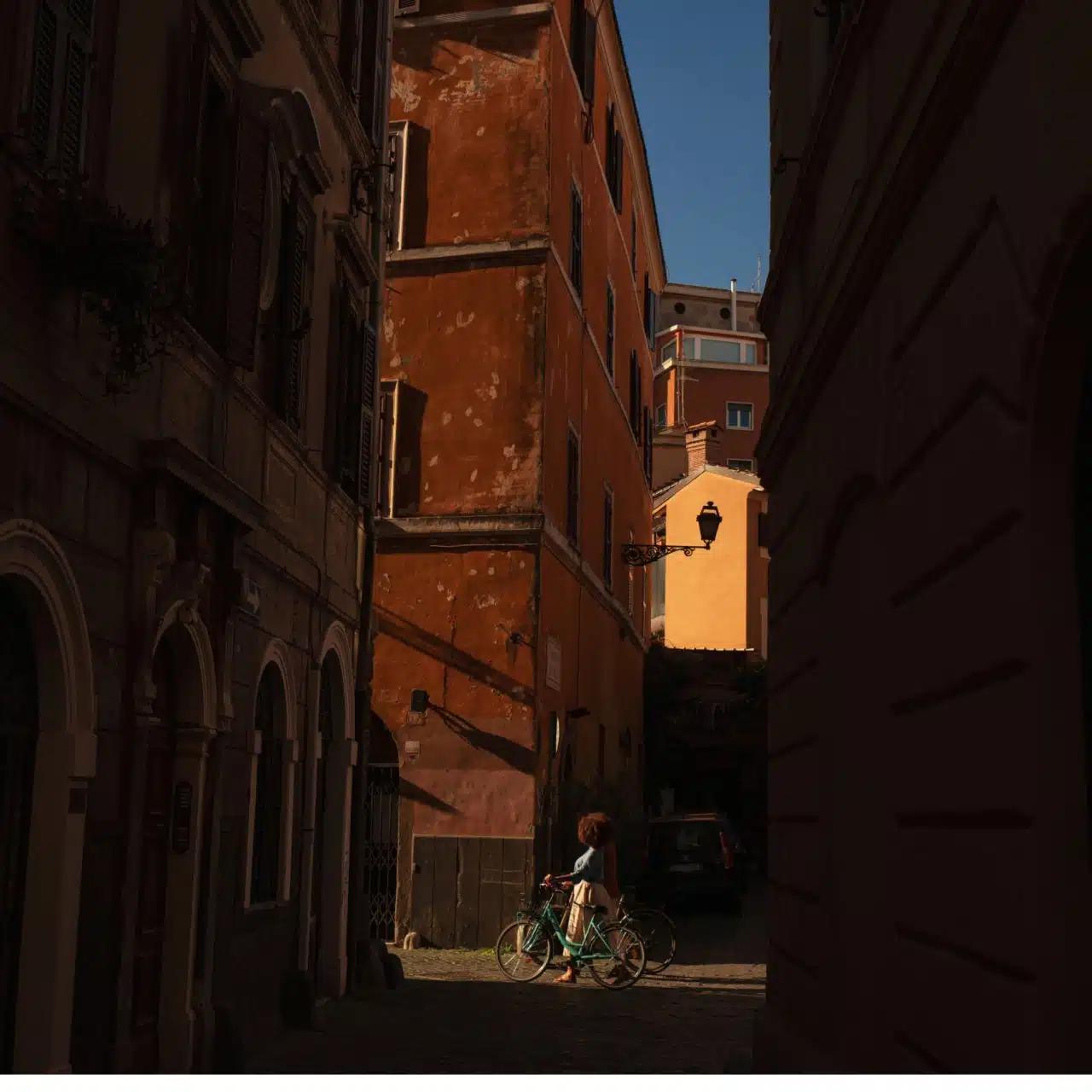 A woman wheeling a bicycle through backstreets is seen at the end of an alley 