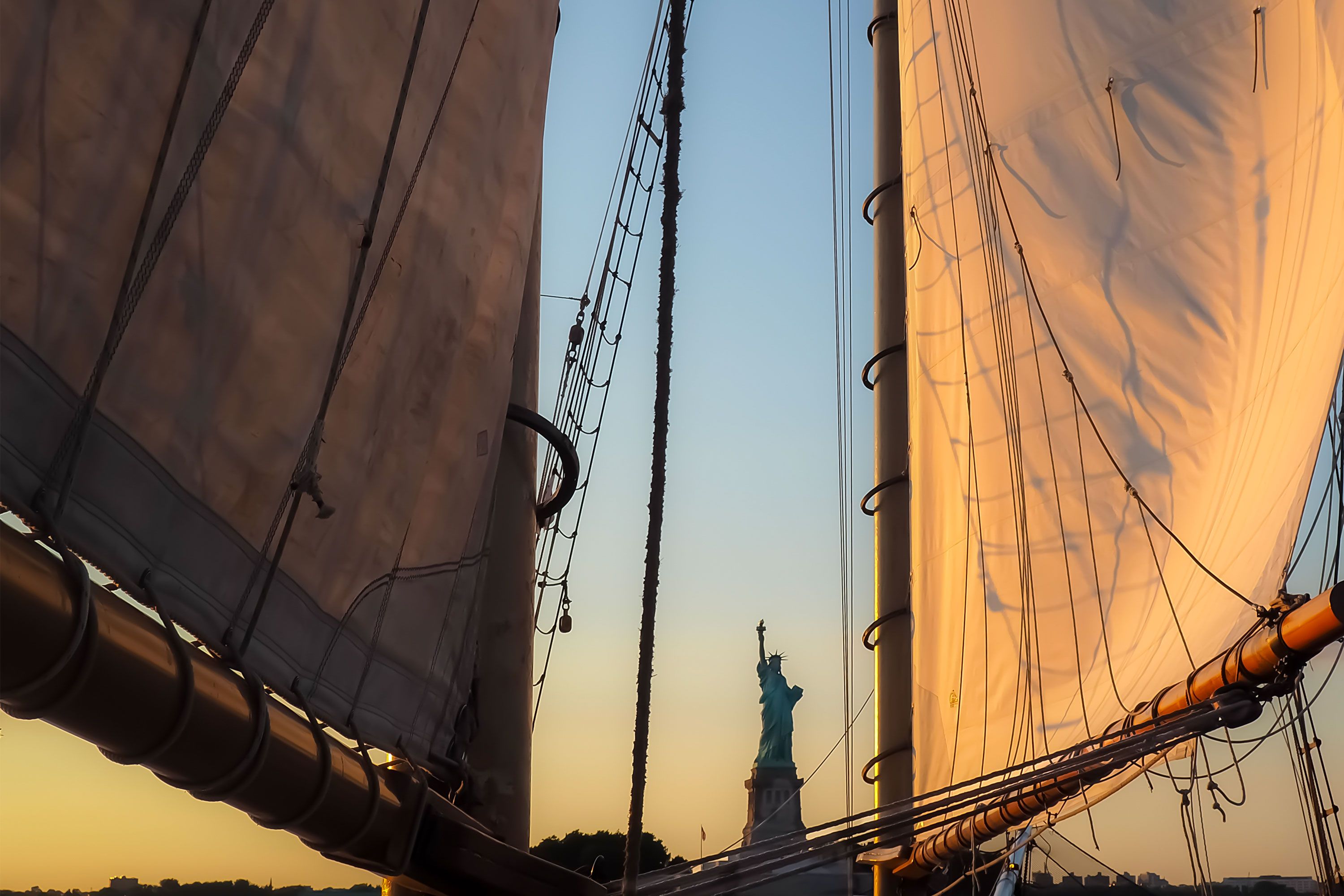 Silhouette of a sailboat on the horizon with a golden-orange sunset sky and calm ocean water.