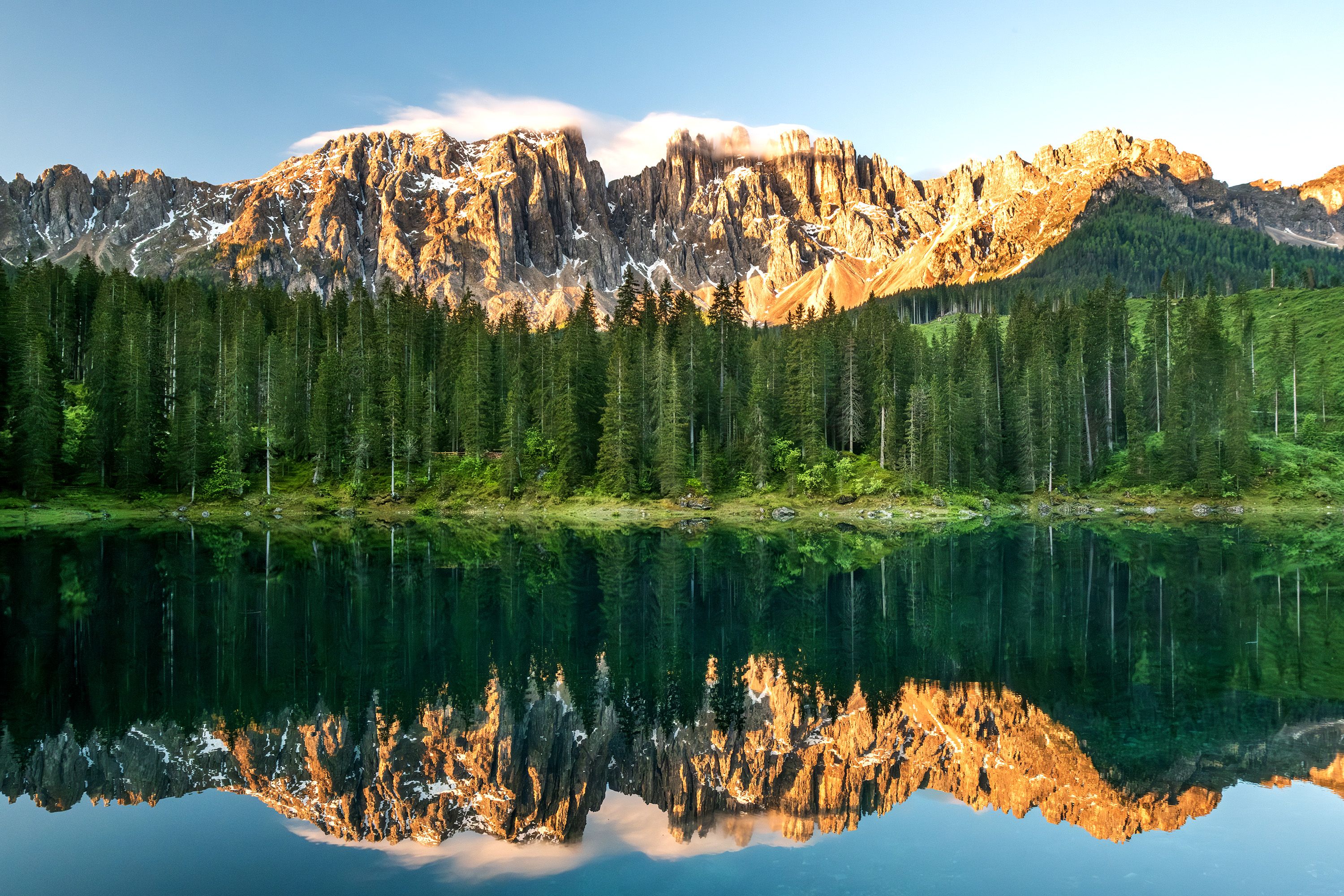 Jagged peaks emerge into the sky above a forest and reflected on water.