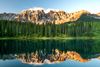 Jagged peaks emerge into the sky above a forest and reflected on water.
