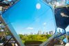 View of Central Park and Manhattan’s skyline seen through the geometric metal and glass structure of a rooftop art installation, with a few visitors visible along the edges.