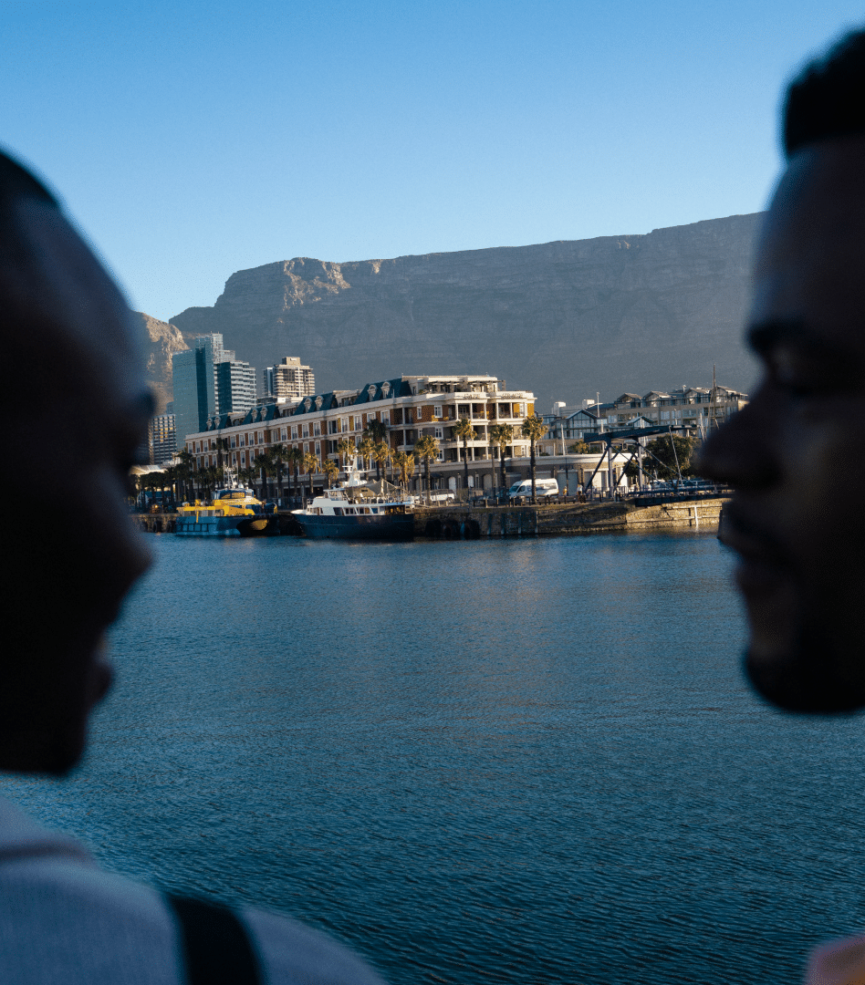 Two people smile at each other, with the V&A Waterfront beyond the water, and Table Mountain above, Cape Town