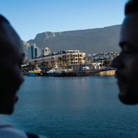 Two people smile at each other, with the V&A Waterfront beyond the water, and Table Mountain above, Cape Town