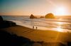 Two people walk along the water's edge at Mile Rock Beach in San Francisco at sunset