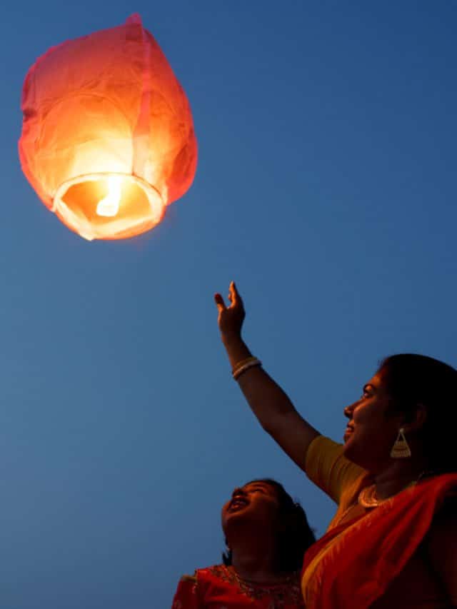 A woman reaches up to a paper lantern in the night sky, India