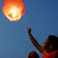 A woman reaches up to a paper lantern in the night sky, India