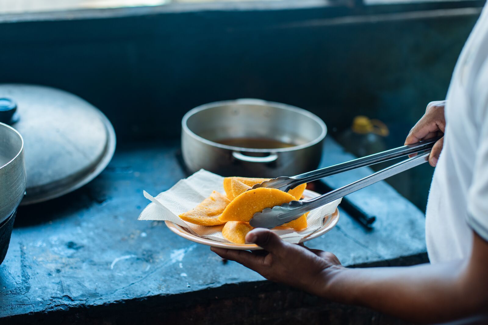 A chef tongs slices of tropical fruit into a pan in a restaurant kitchen in Panama City