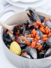A light grey cast iron dish is filled with fresh mussels topped with chopped tomatoes and a wedge of lemon in Italy