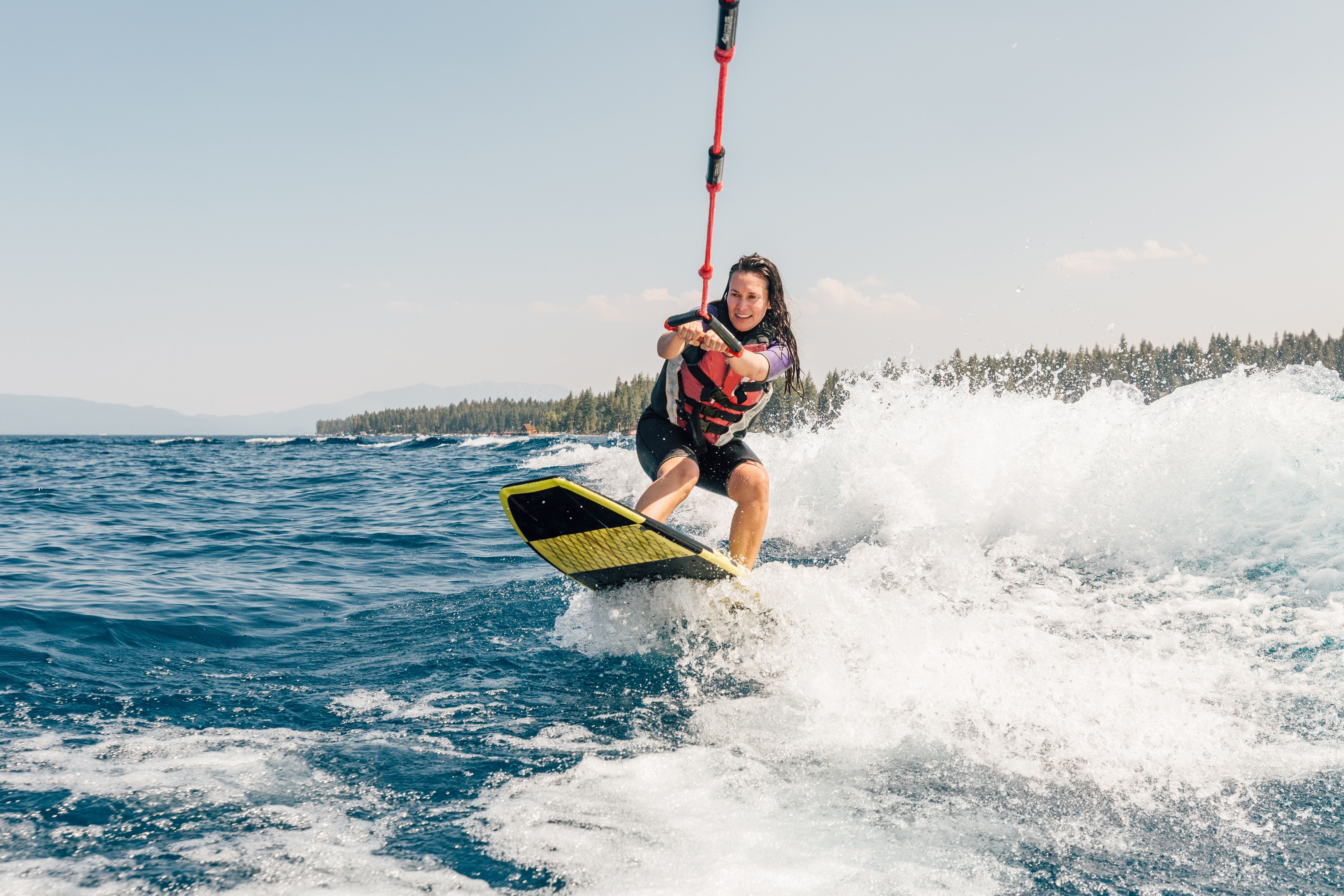 A woman with long brunette hair wakeboards over choppy waters