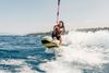 A woman with long brunette hair wakeboards over choppy waters