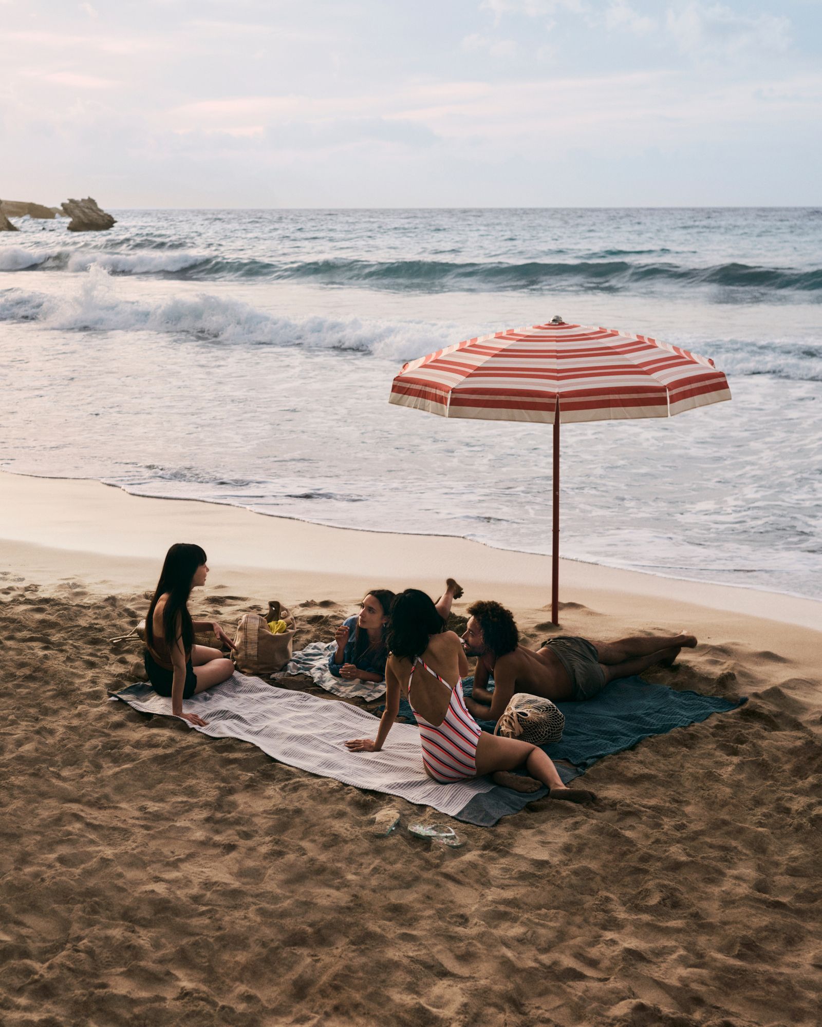 A group of women sit on towels on a beach with waves lapping nearby