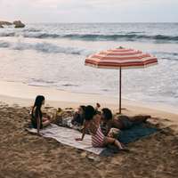 A group of women sit on towels on a beach with waves lapping nearby