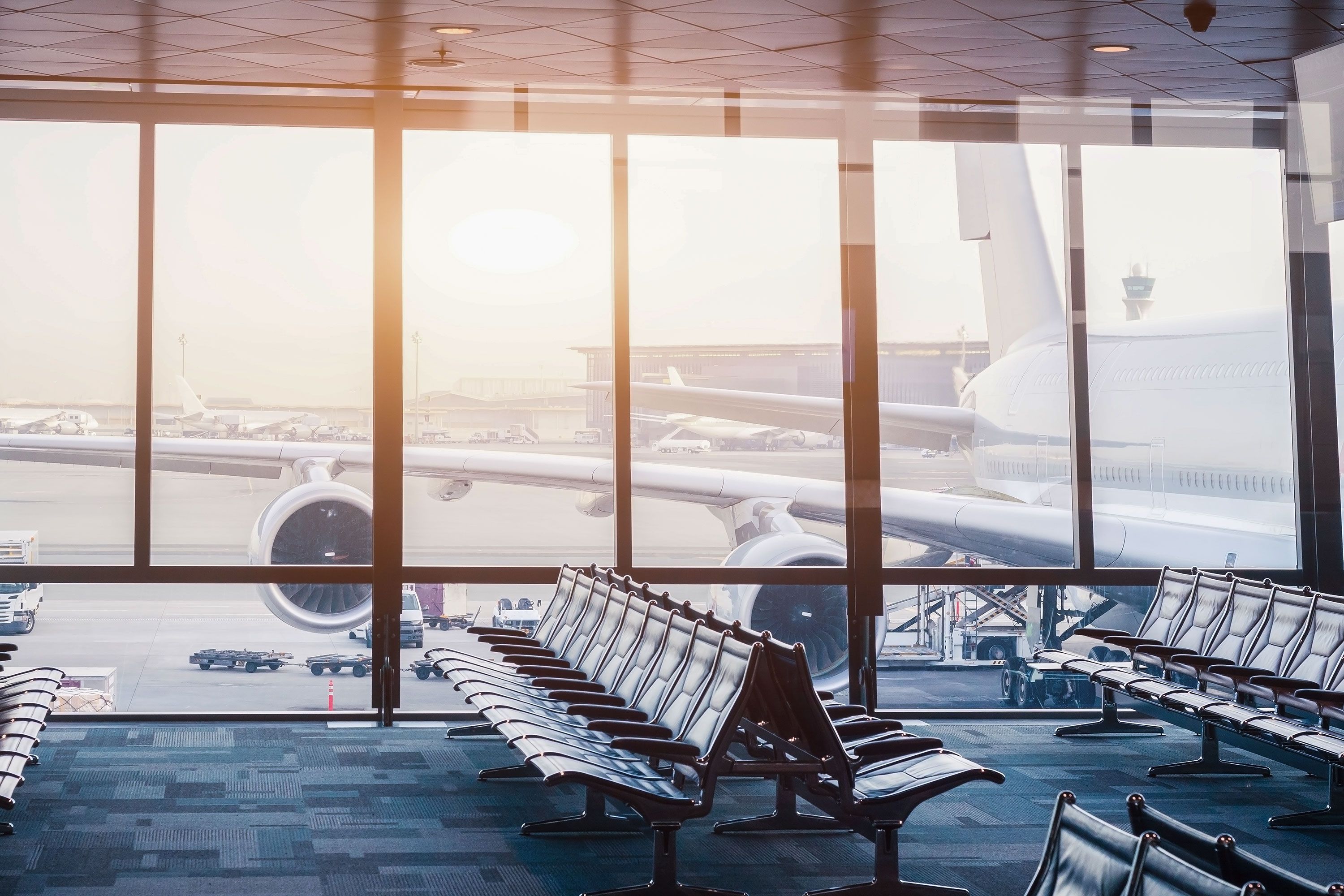 Rows of chairs at an airport boarding gate in front of a floor-to-ceiling window, with an aircraft visible outside