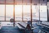 Rows of chairs at an airport boarding gate in front of a floor-to-ceiling window, with an aircraft visible outside