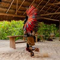 A person in a traditional colorful feathered headdress performs on the beach as part of a ceremony in Tulum, Mexico