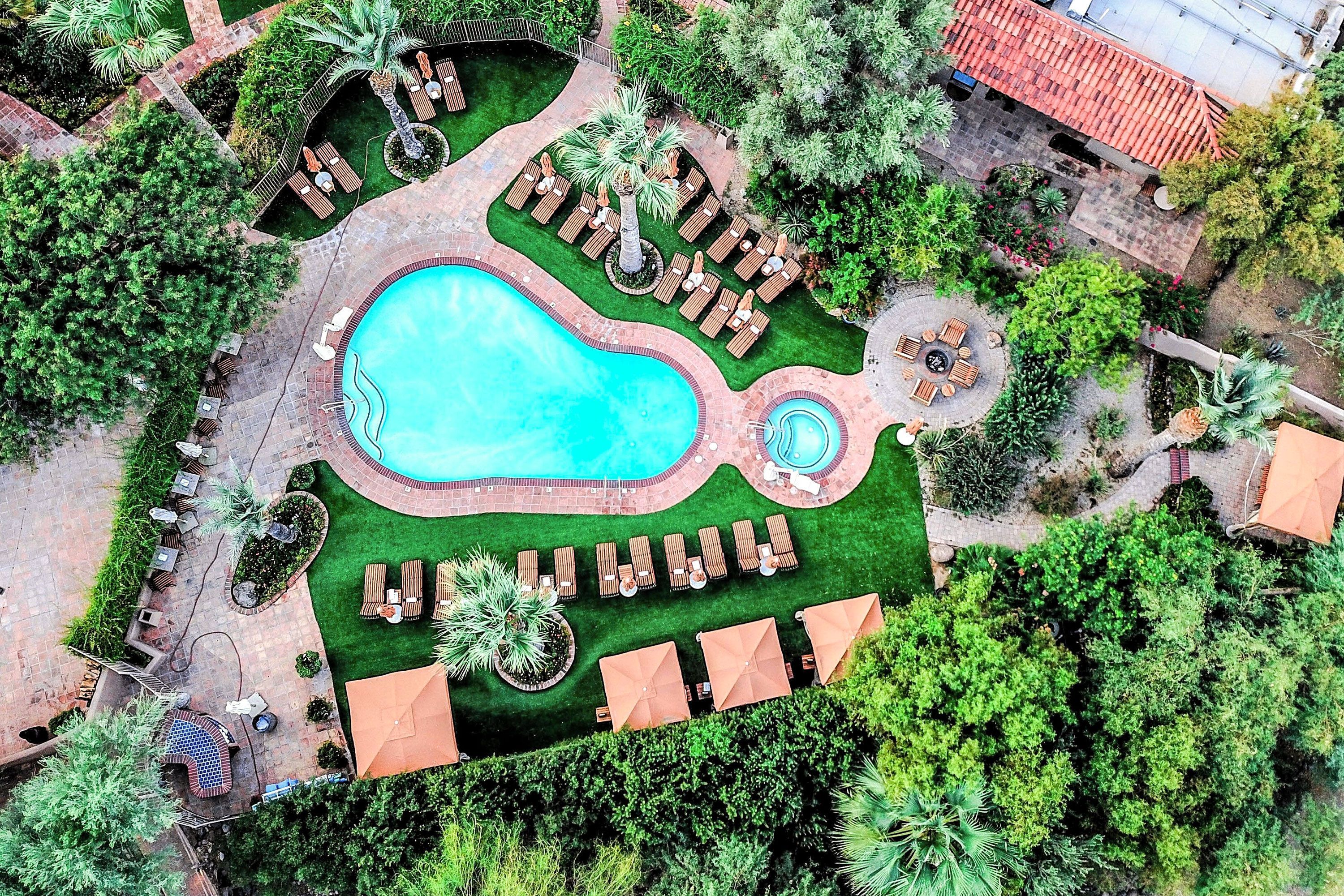 Overhead view of pear-shaped pool and jacuzzi surrounded by lounge chairs, paths and vegetation.
