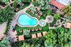 Overhead view of pear-shaped pool and jacuzzi surrounded by lounge chairs, paths and vegetation.