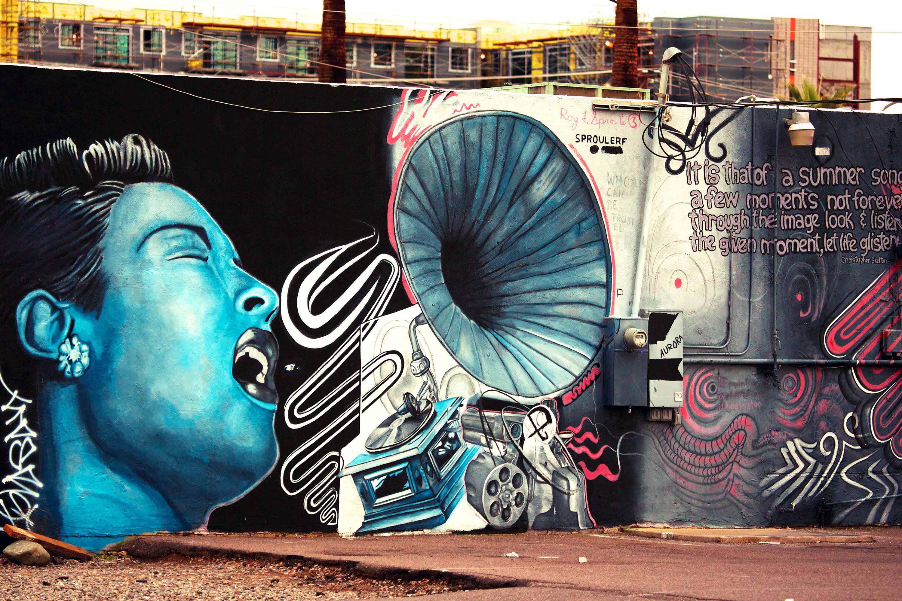 Colorful mural showing a stylized blue portrait of a singer next to a large gramophone, record player, and swirling musical designs painted on an exterior wall.