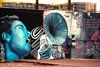 Colorful mural showing a stylized blue portrait of a singer next to a large gramophone, record player, and swirling musical designs painted on an exterior wall.