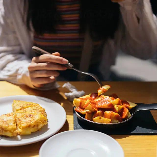 A diner in a striped shirt tucks into a dish of patatas bravas and tortilla