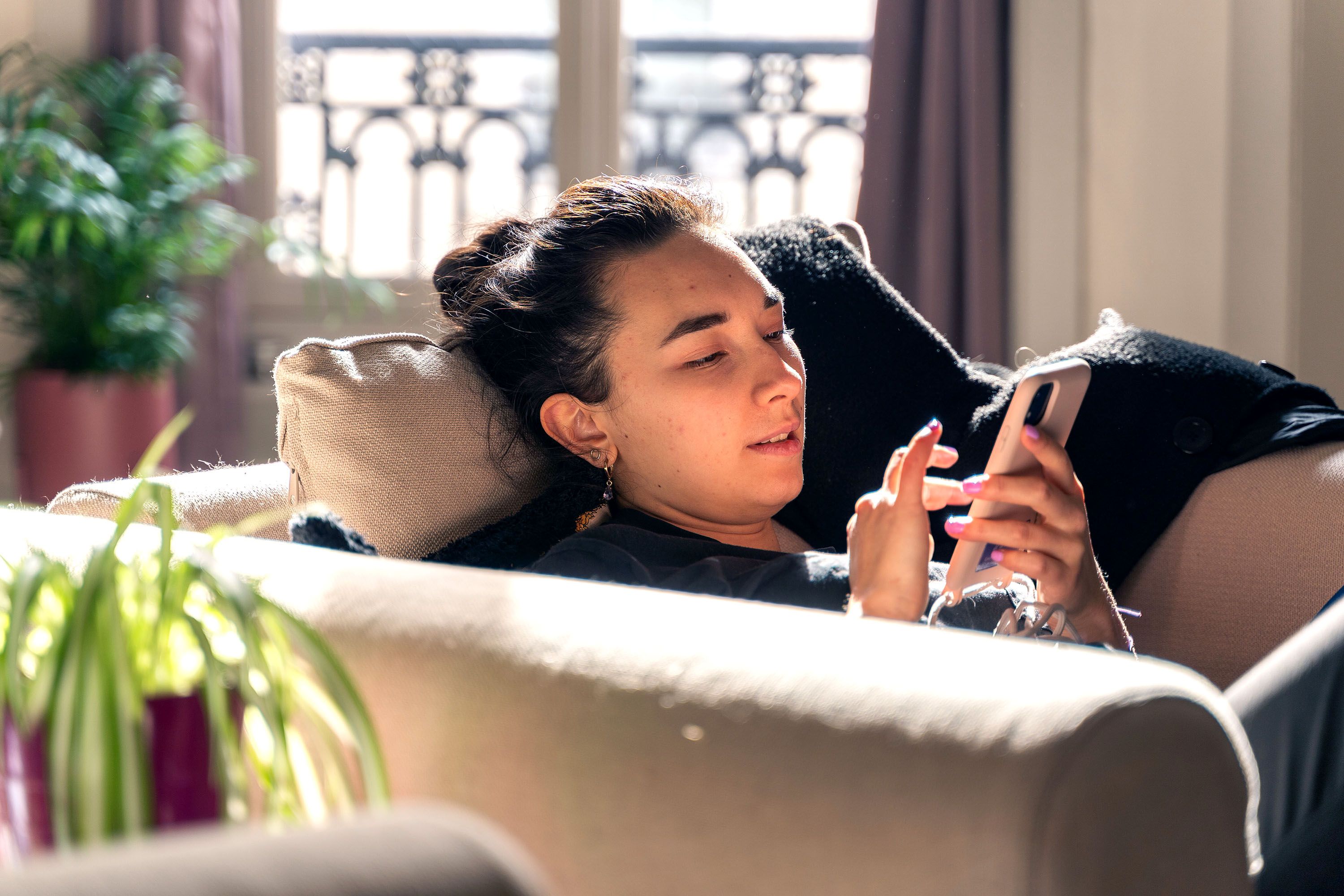Person sits on a sofa and scrolls on their cellular phone.
