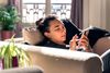 Person sits on a sofa and scrolls on their cellular phone.
