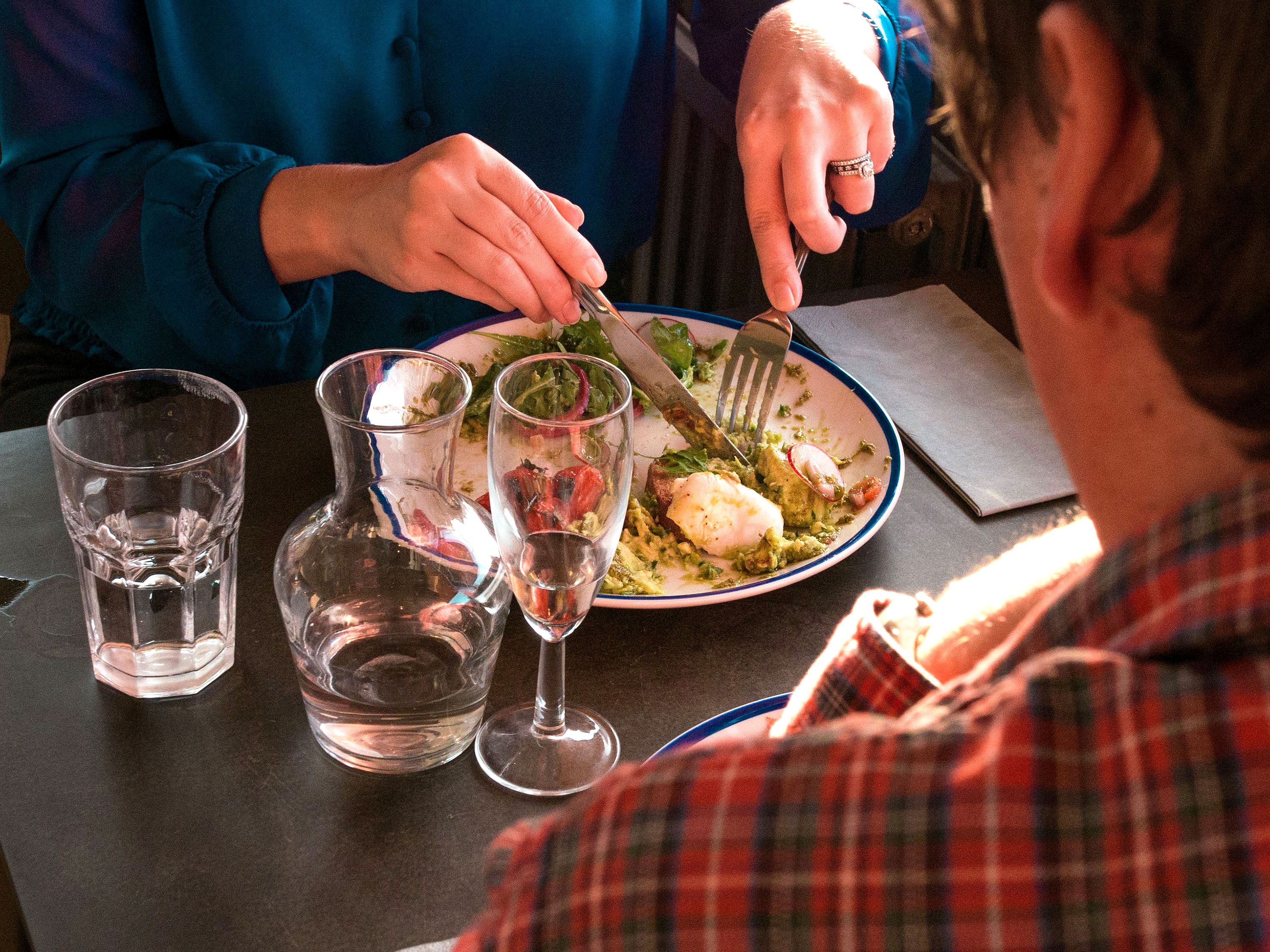 Two people sit at a table in a restaurant as on cuts their food.