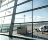 Looking out a window from an airport gate area to a plane taking off and another plane attached to a jetway.