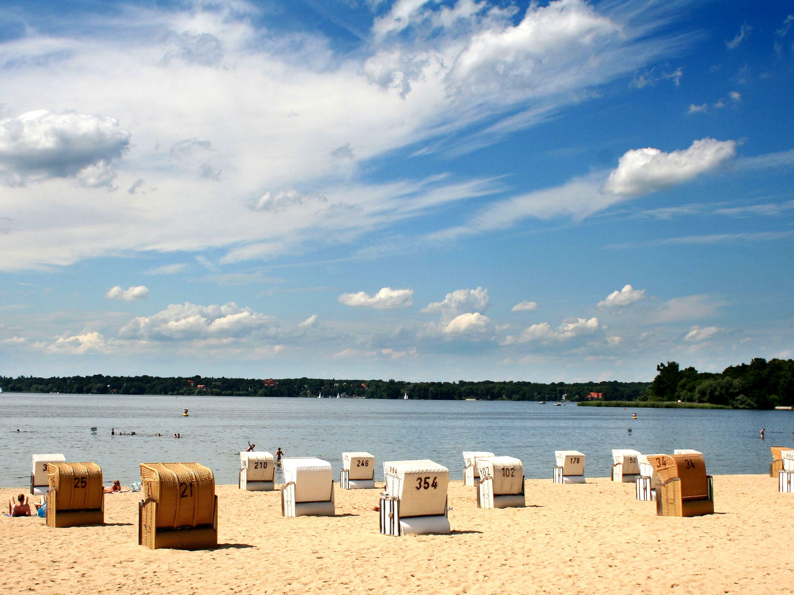 White and brown beach chairs on sandy beach and a partly cloudy sky.