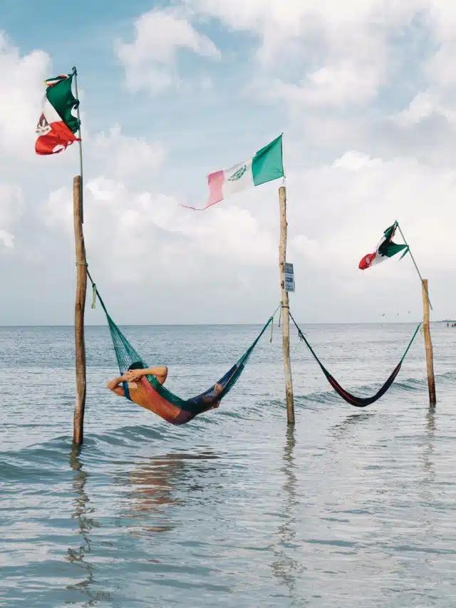 A person lounges in a hammock strung between flagpoles in the sea