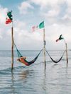 A person lounges in a hammock strung between flagpoles in the sea