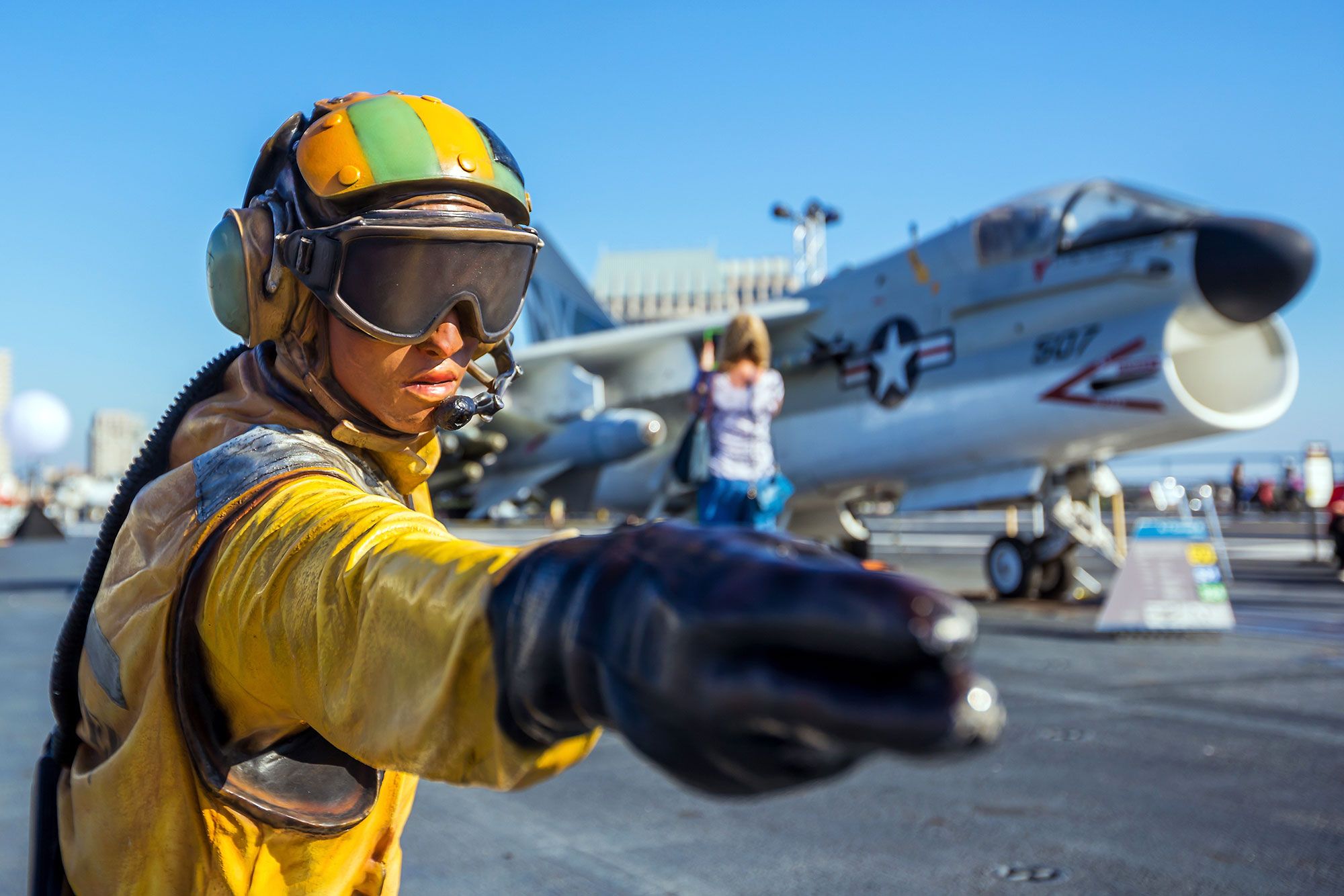 A statue of a pilot pointing his arm and fingers forward with a fighter jet in the background.