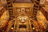 A close-up view of a lavishly decorated theater ceiling with detailed carvings, gold accents, and a hanging antique chandelier.