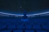 Interior view of darkened planetarium with seating and projector and stars on ceiling.