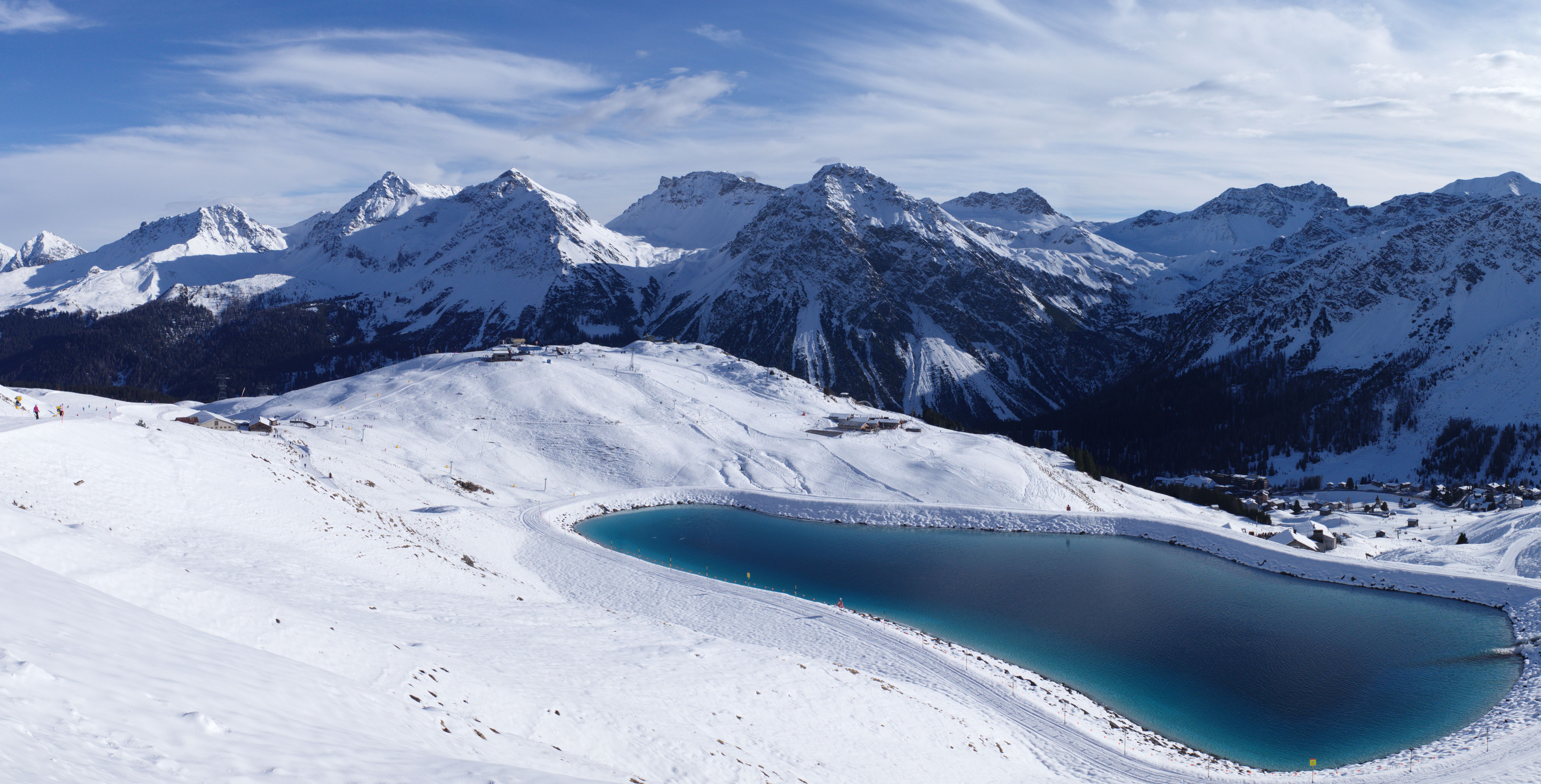 A turquoise reservoir sits in a bowl of pisted snow, ringed by the peaks of the Plessur Alps.
